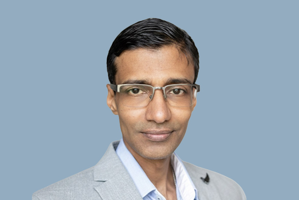 Image of a man wearing a silver coat with a white shirt inside. he is also wearing a specs and the picture is taken on the background of a blue screen
